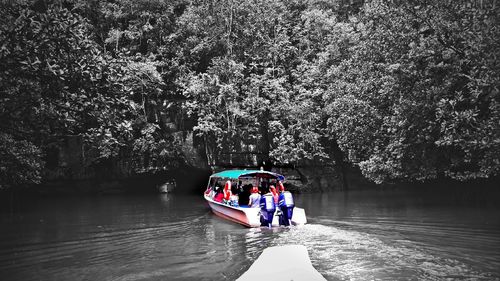 People on boat in river against trees