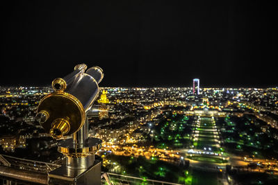 Coin-operated binoculars against illuminated cityscape against sky at night