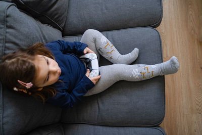 High angle view of girl playing video game while sitting on sofa at home