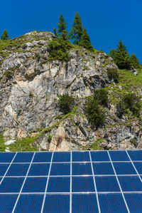 Solar photovoltaic panels against the backdrop of rocky mountains covered with green plants trees