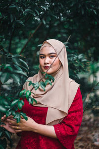 Portrait of young woman standing against plants