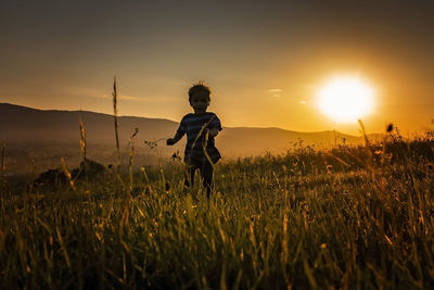 Side view of woman standing on field against sky during sunset