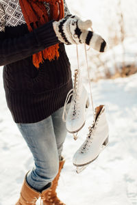 Midsection of woman holding ice skates while standing on frozen lake