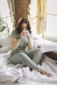 Young woman sitting on bed at home