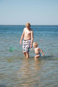 Rear view of shirtless boy in sea against clear sky