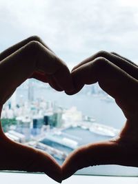 Close-up of person hand making heart shape against sky