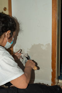 Rear view of woman painting with putty knife while sitting at home