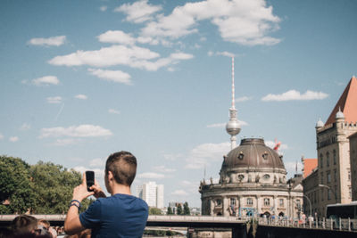 Rear view of man photographing in city with fernsehturm in background