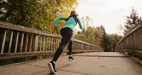 Young woman on running on footbridge against sky