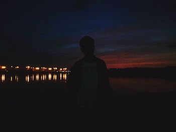 Rear view of silhouette man standing against illuminated sky at sunset