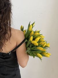 Rear view of woman standing by sunflower against wall