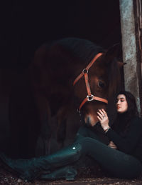 Woman sitting with horse at stable