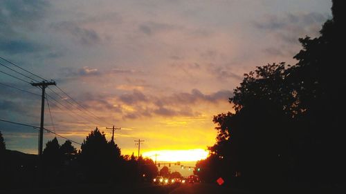 Silhouette trees and electricity pylon against sky during sunset