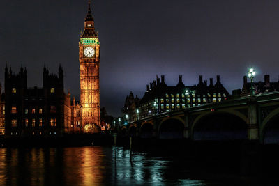 Illuminated tower bridge over river and buildings against sky at night