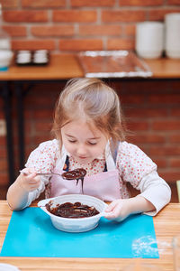 Girl smelling batter on table at home