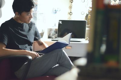 Man reading book while sitting on chair at home