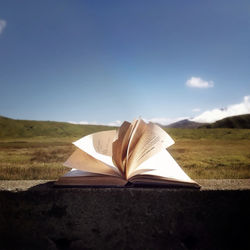 Open book against countryside landscape and blue sky