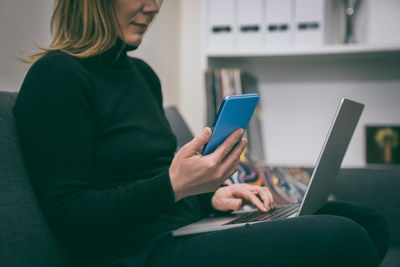 Midsection of woman using phone while sitting on sofa at home