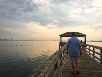 Rear view full length of man walking on pier over lake against sky