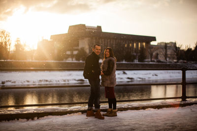 Full length of couple standing at shore against sky during winter