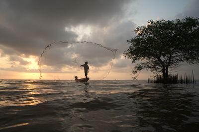 Man fishing in sea against sky during sunset