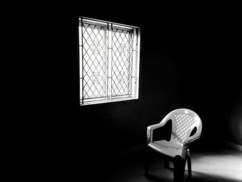 A dark room with a single light source , a horrific place , psychotic room . chair opposite to windo