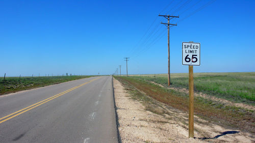 Speed limit 65 sign and electricity pylon by country road against clear blue sky