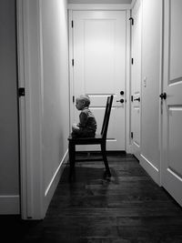 Boy sitting on wooden chair at hallway