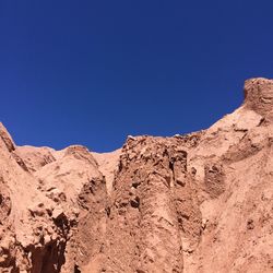 Low angle view of rocky mountains against clear blue sky