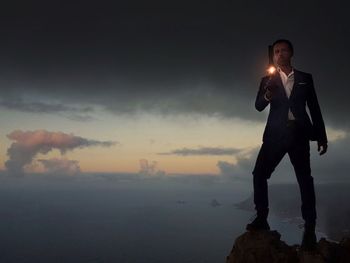 Full length of man holding lantern while standing on cliff against sky