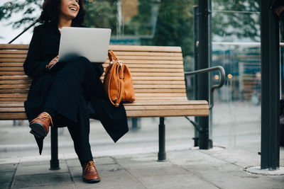 Full length of woman using mobile phone while sitting on bench