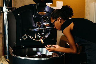 Young woman with roasted coffee beans by machinery