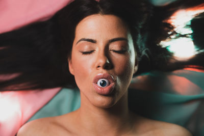 High angle view of woman with eyeball in mouth lying on bed at home