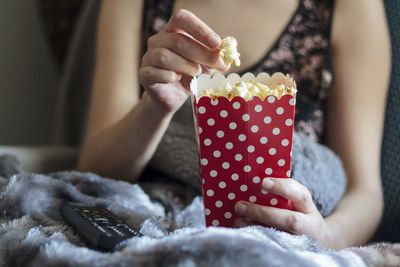 Woman at home wrapped in warm blanket and eating popcorns