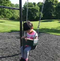 Full length of cute baby girl sitting on swing against trees