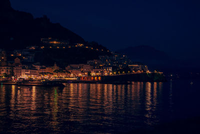 Illuminated buildings by river against sky at night