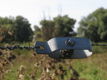 Close-up of metal fence on field against sky