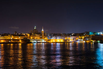 Illuminated cityscape by river against sky at night