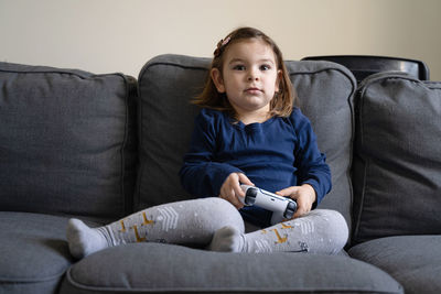 Full length of girl holding game controller sitting on sofa