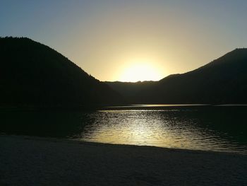 Scenic view of lake by silhouette mountains against clear sky