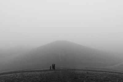 People on mountain against sky during foggy weather