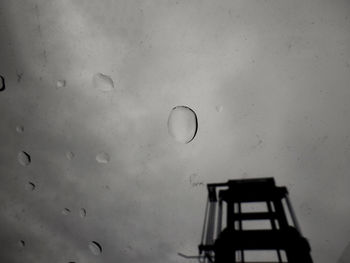 Low angle view of wet glass window against sky