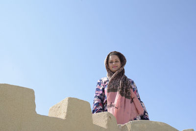 Low angle portrait of woman against clear blue sky