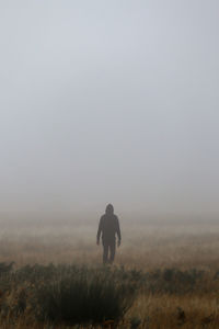 Rear view of man walking on field against clear sky