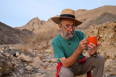 Portrait of senior man drinking water while standing on mountain