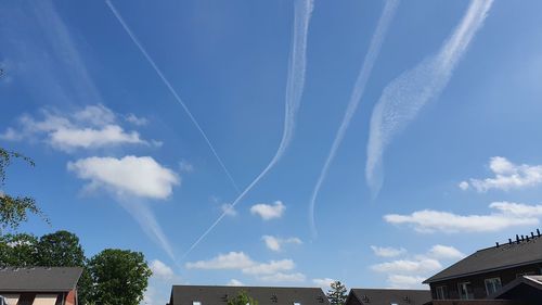 Low angle view of vapor trails over buildings against sky