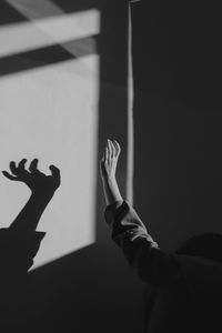 Woman with raised hand standing by shadow on wall