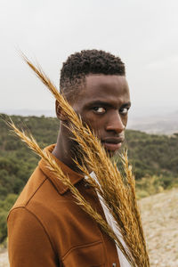 Serious african american male with bunch of dried wheat standing in nature and looking away