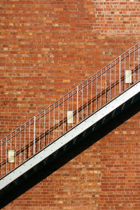 An empty fire escape stairs on the building exterior, red brick wall background.