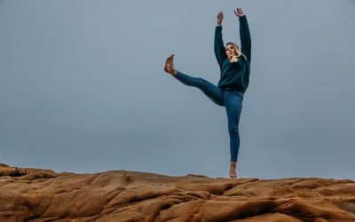 Low angle view of woman with arms raised standing on mountain against sky